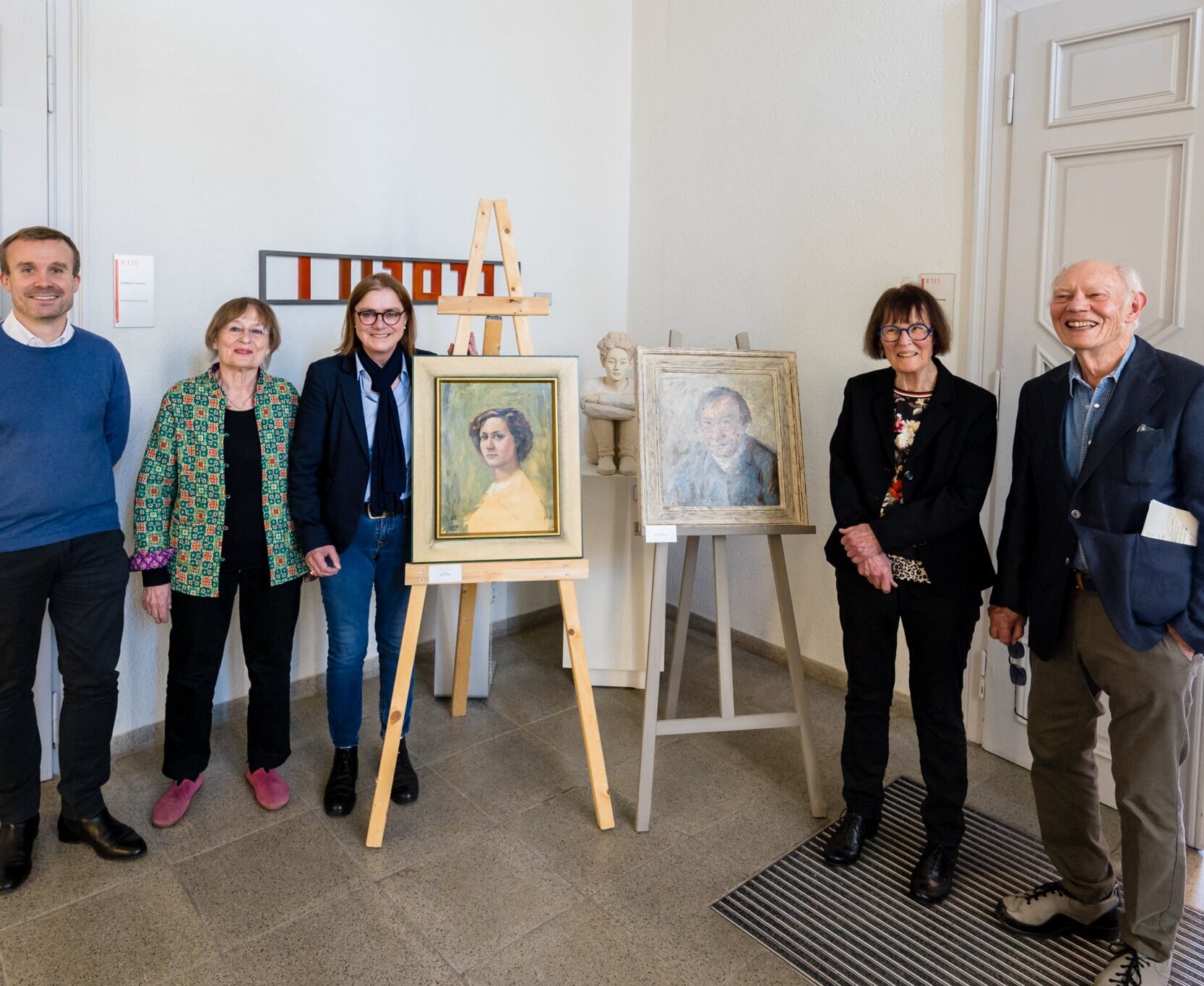 Die Portraits von Gerda Schneider (gemalt von Hardy Schneider-Sato, 1952) und Hardy Schneider-Sato (gemalt von Oskar Hagemann) – zur linken Seite: Ferdinand Leikam, Leiter der Historischen Museen der Stadt Karlsruhe, Kulturbeiratsmitglied Hildegund Brandenburg (Mitte) und Ortsvorsteherin Alexandra Ries; zur rechten Seite: Kulturbeiratsmitglied Erika Rödiger-Diruf und Wegbegleiter Eckhart Pilick. 