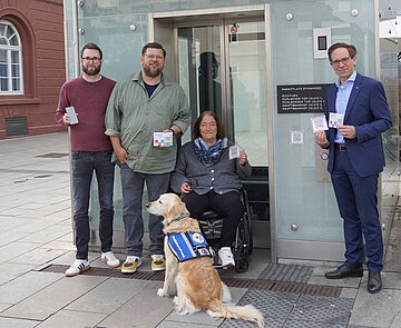 Am Karlsruher Marktplatz testen (v.l.n.r.) Christian Höglmeier (technischer Geschäftsführer der VBK), Ulrike Wernert (kommunale Behindertenbeauftragte der Stadt Karlsruhe), Artur Bundnik (Projektstelle Web-App „Karlsruhe barrierefrei“) und Marcus Albert (System-Administrator „Karlsruhe barrierefrei“) die neuen QR-Codes an den Stadtbahntunnel-Aufzügen, über die die Nutzer*innen schnell und direkt auf die Seite „Karlsruhe barrierefrei“ gelangen.