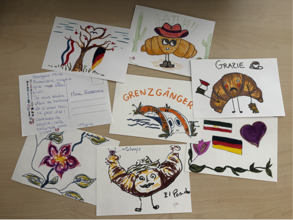 Bunte Postkarten mit deutsch-französischen Motiven auf einem Tisch.