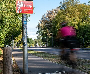  Blick auf den Fahrradstreifen am Adenauerring mit Hinweisschild auf Geisterradler und Fahrradfahrer der entgegen der zulässigen Fahrtrichtung auf dem Radfahrstreifen unterwegs ist.
