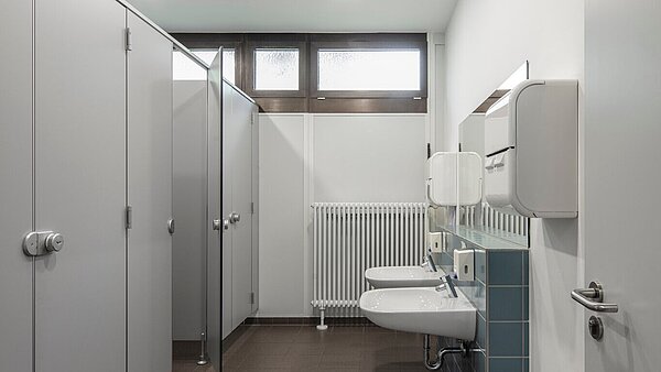 Das Bild zeigt das rundum erneuerte WC mit Gipskartondecke, neuen Fliesen und einem modernen Trennwandsystem in schlichten Farben.