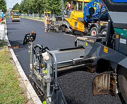 Bei der Baustelle an der Ludwig-Erhard-Allee wird zur Fahrbahnsanierung ein neuartiger Niedertemperaturasphalt auf der Fahrbahn aufgebracht.