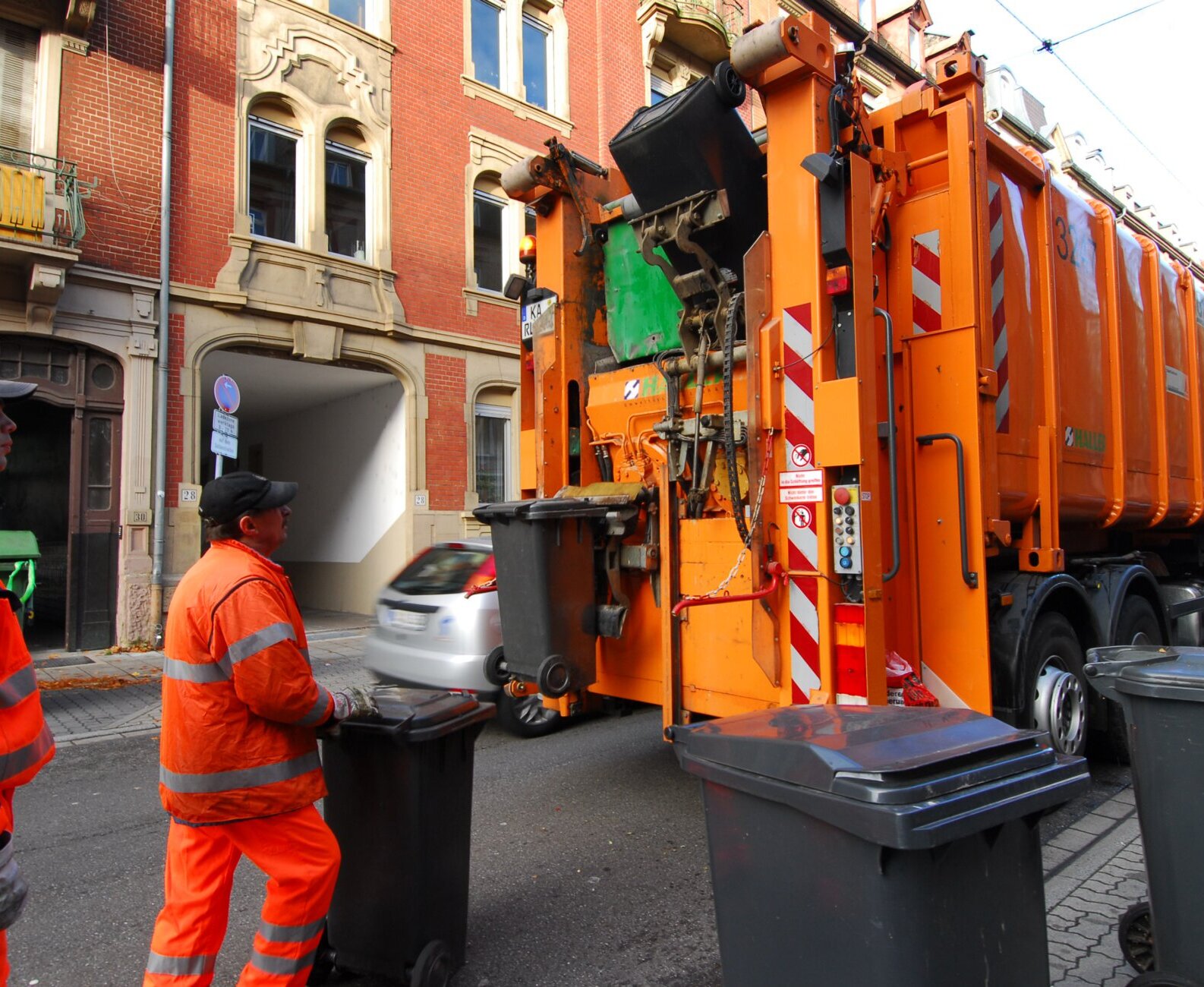 Zwei Müllmänner bringen Mülltonnen zu einem Müllfahrzeug.