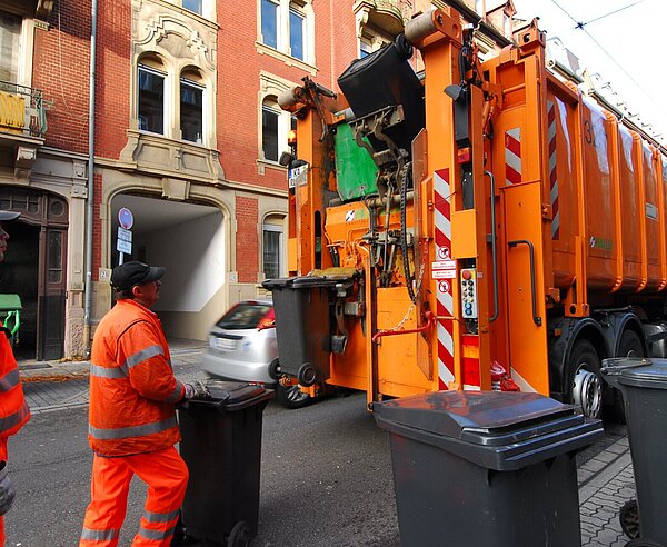 Zwei Müllmänner bringen Mülltonnen zu einem Müllfahrzeug.