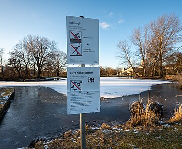 Zugefrorene Teiche in der Günther-Klotz-Anlage am Nachmittag mit Verbotsschild Tiere zu füttern , zu schwimmen und die Eisfläche zu betreten