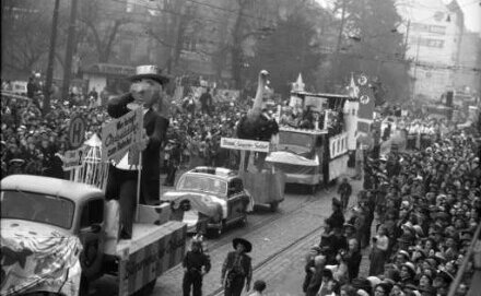 Umzug mit Blick auf mehrere Wagen, gesäumt von der Menge der Zuschauenden. 