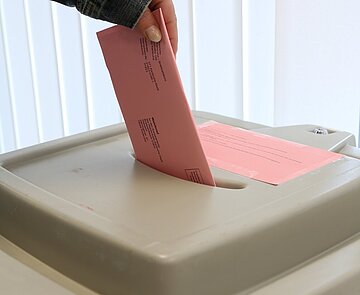 Person wirft Briefwahlumschlag in eine Wahlurne