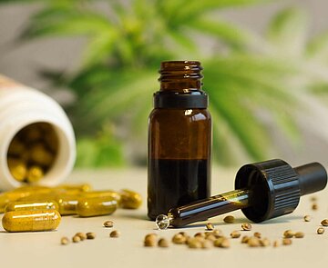 Kapseln, Tinkturen und Hanfsamen vor einer Cannabispflanze