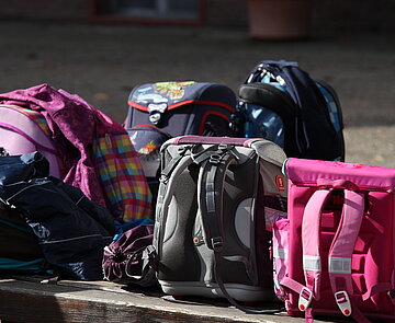 Mehrere Schulranzen stehen auf einer Bank