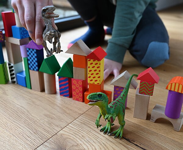Bild spielt mit Dinosaurier und Bauklötzen.