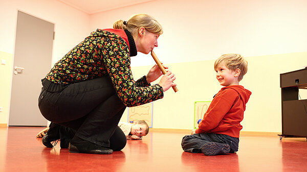 Musiklehrerin zeigt Kleinkind Flötenspiel.