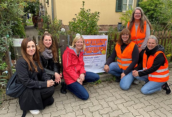 Die Kinderbeauftragte Jessica Schöllhorn, Kinderinteressenvertretung Christina Schulze, Bürgermeisterin Yvette Melchien und Patinnen aus der Nordstadt: Gitta Langer, Alexandra Boltz, Stephanie Of, posieren knieend vor einem Gartenzaun mit Plakat zur Aktion Karlsruhe spielt