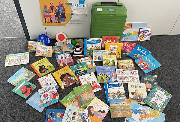 KinderrechtekofferPLUS, davor eine Auswahl von Büchern, Spielen und Materialien zu den Themen Kinderschutz und Kinderrechte.  