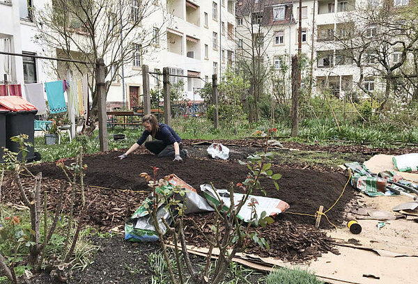 Hinterhofgarten Frau verteilt frische Erde auf neuem Beet