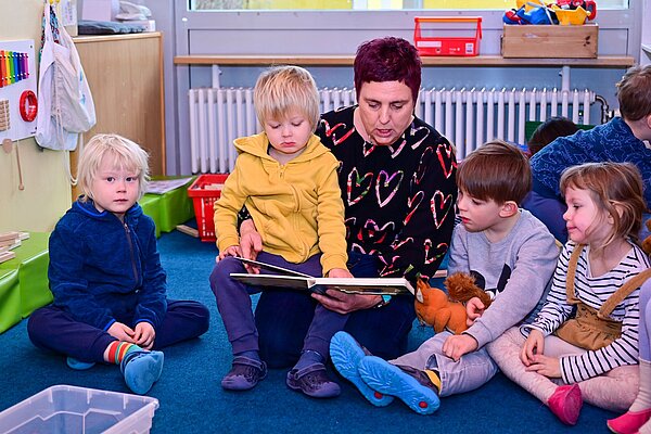 Eine Erzieherin liest mit vier Kindern ein Buch.