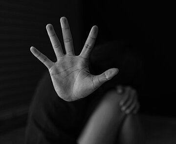 Person hockt auf Boden und hält Hand als Schutz vor Gesicht und Körper. 