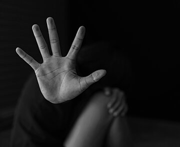 Person hockt auf Boden und hält Hand als Schutz vor Gesicht und Körper. 