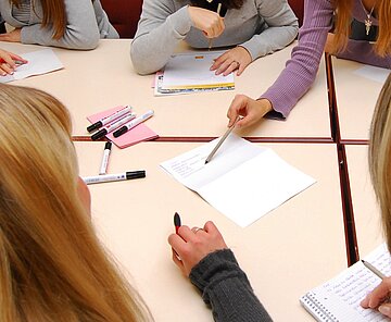 Person zeigt am Tisch mit Schreibgerät auf ein Schriftstück.
