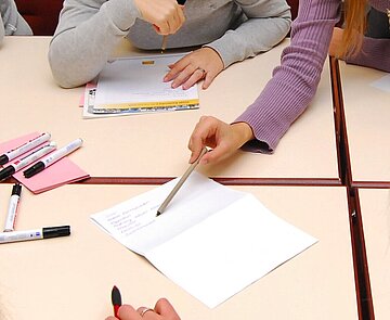 Person zeigt am Tisch mit Schreibgerät auf ein Schriftstück.