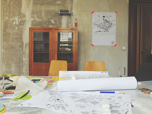 Tisch in einem Raum mit verschiedenen Plänen, Skizzen und Schreibutensilien