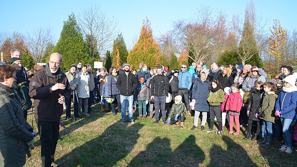 Personen auf einer Wiese, die im Halbkreis stehen und einer Ansprache zuhören