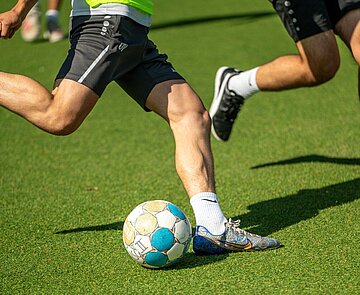 Nahaufnahme von Beinen und einem Fußball auf einem Bolzplatz