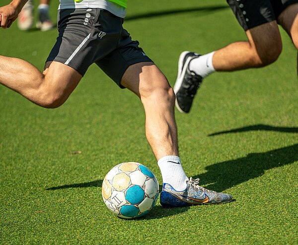 Nahaufnahme von Beinen und einem Fußball auf einem Bolzplatz