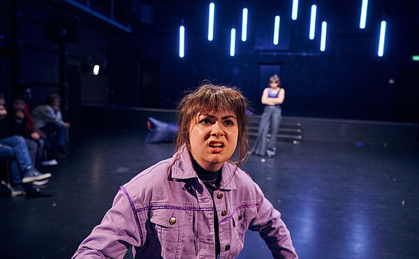 Szene aus dem Theaterstück, junge Frau in lila Jacke