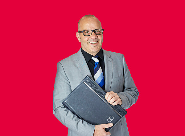 Mann steht mit Dokumentenmappe in der Hand vor rotem Hintergrund