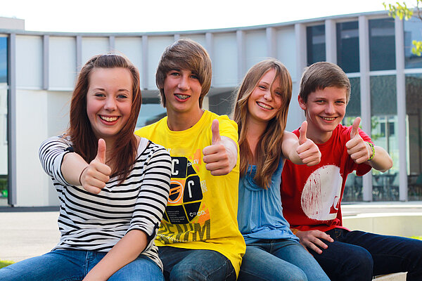 Vier Jugendliche, die in die Kamera lachen und Daumen nach oben zeigen.