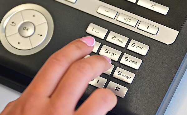 Das Bild zeigt ein Telefon mit der Hand einer Person, die eine Notfallnummer wählt.