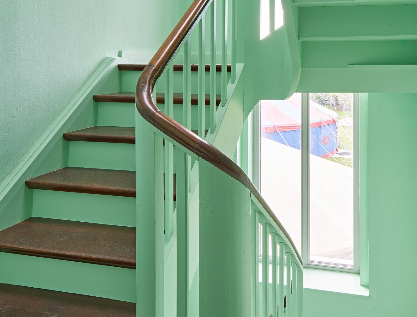 Das Bild zeigt das Treppenhaus mit hellgrünem Anstrich mit Holzfußboden und -stufen.
