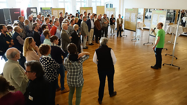 Personen, die im Halbkreis stehen und dem Moderator zuhören