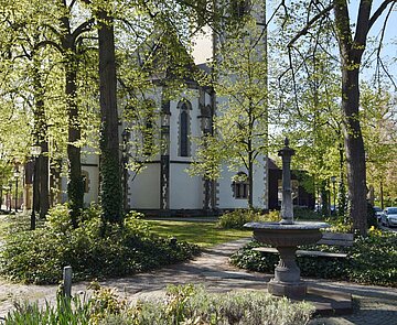 Ein Brunnen mit Kirche und Bäumen im Hintergrund.