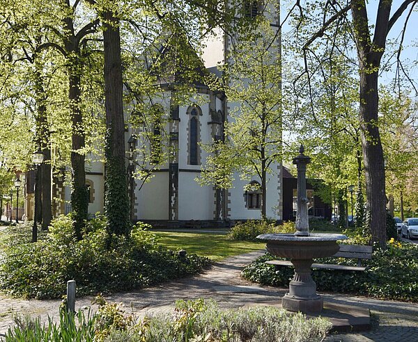 Ein Brunnen mit Kirche und Bäumen im Hintergrund.