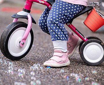 Kind mit Dreirad steht auf Straße