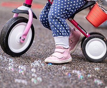 Kind mit Dreirad steht auf Straße