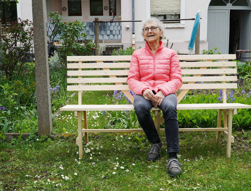 Marianne sitzt lachend auf der fertigen Bank im Garten.
