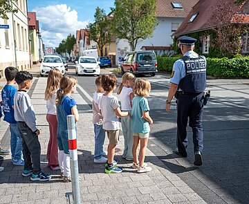Eine Gruppe Schulkinder übt mit einem Beamten der Polizei die sicherer Überquerung einer Straße.
