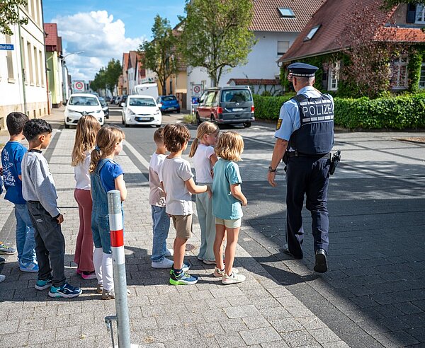 Eine Gruppe Schulkinder übt mit einem Beamten der Polizei die sicherer Überquerung einer Straße.