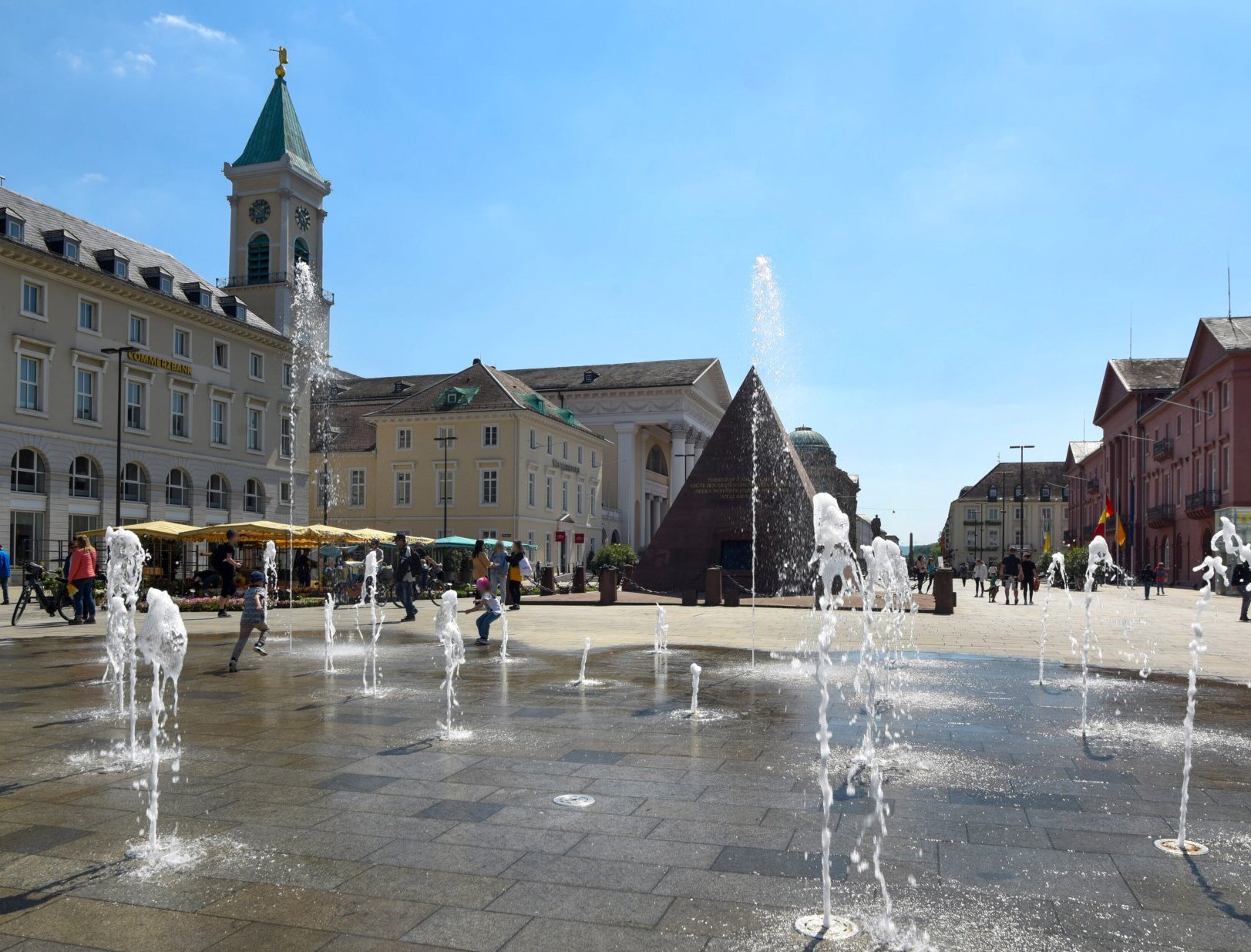 belebter Marktplatz mit Menschen und Wasserspiel im Sommer