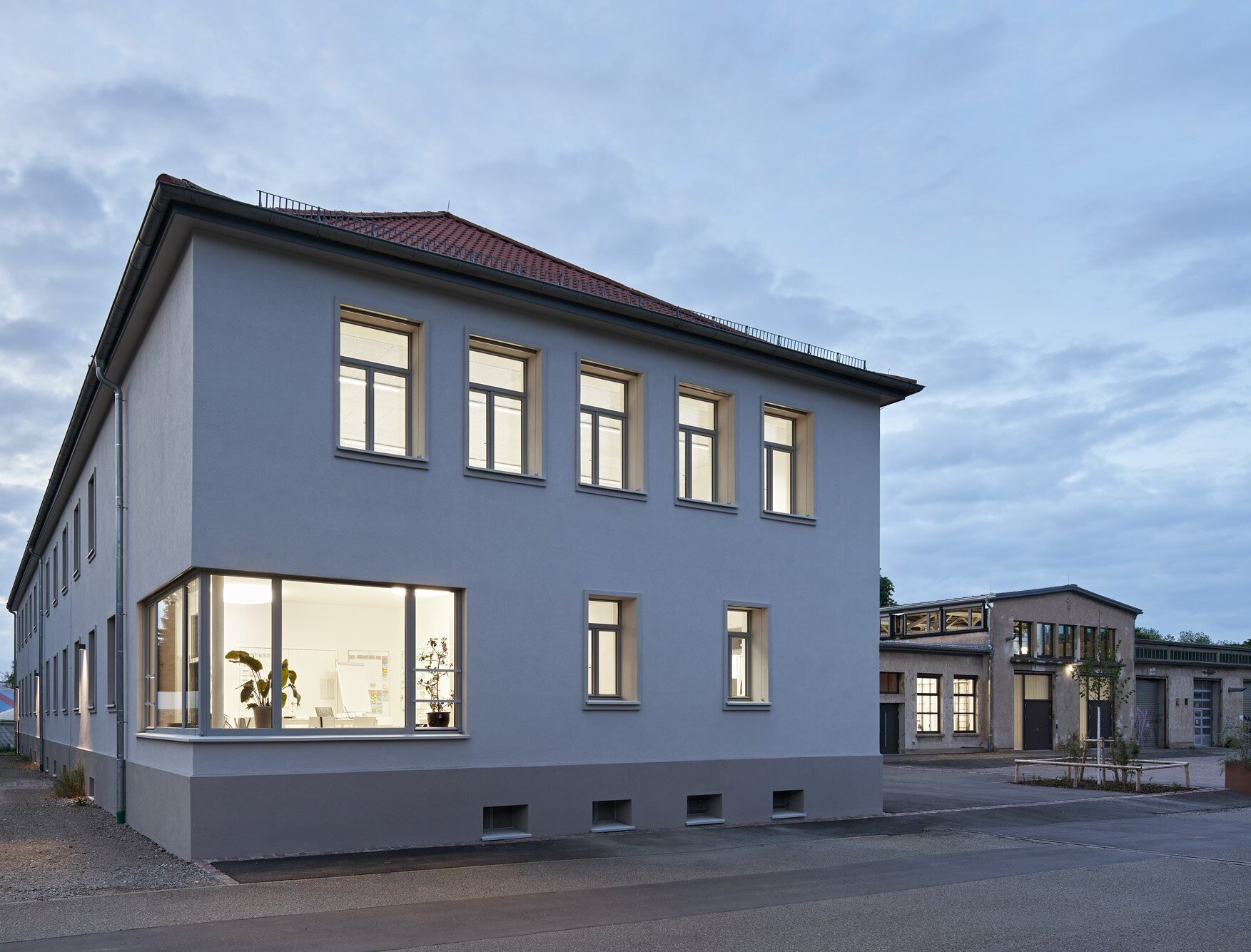 Zu sehen ist die beleuchtete Südostfassade des Verwaltungsgebäudes mit markantem Eckfenster in der Dämmerung.