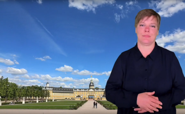 Screenshot eines Videos; eine Person spricht vor der Bild des Schloss Karlsuhe