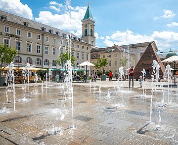 neugestalteter, belebter Marktplatz mit Wasserspiel, Bäume in Kübeln bei sommerlicher Atmosphäre