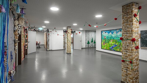 Das Bild zeigt den Flurbereich im Kellergeschoss mit neuem grauen Boden, heller Akustikdecke und energieeffizienten LED-Leuchten. Die Dekoration wirkt freundlich und naturnah.
