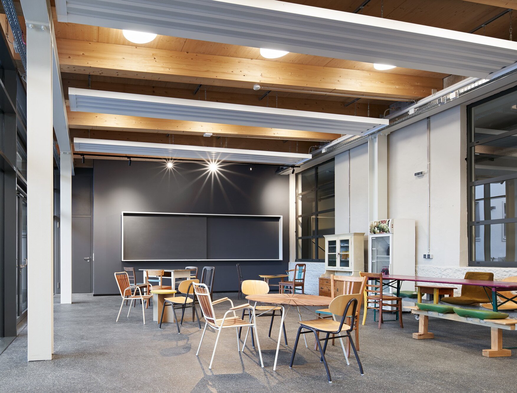 Zu sehen ist die Kantine mit Holzdecke und grauen Akzenten sowie mit einer vielfältigen, individuellen Möblierung.