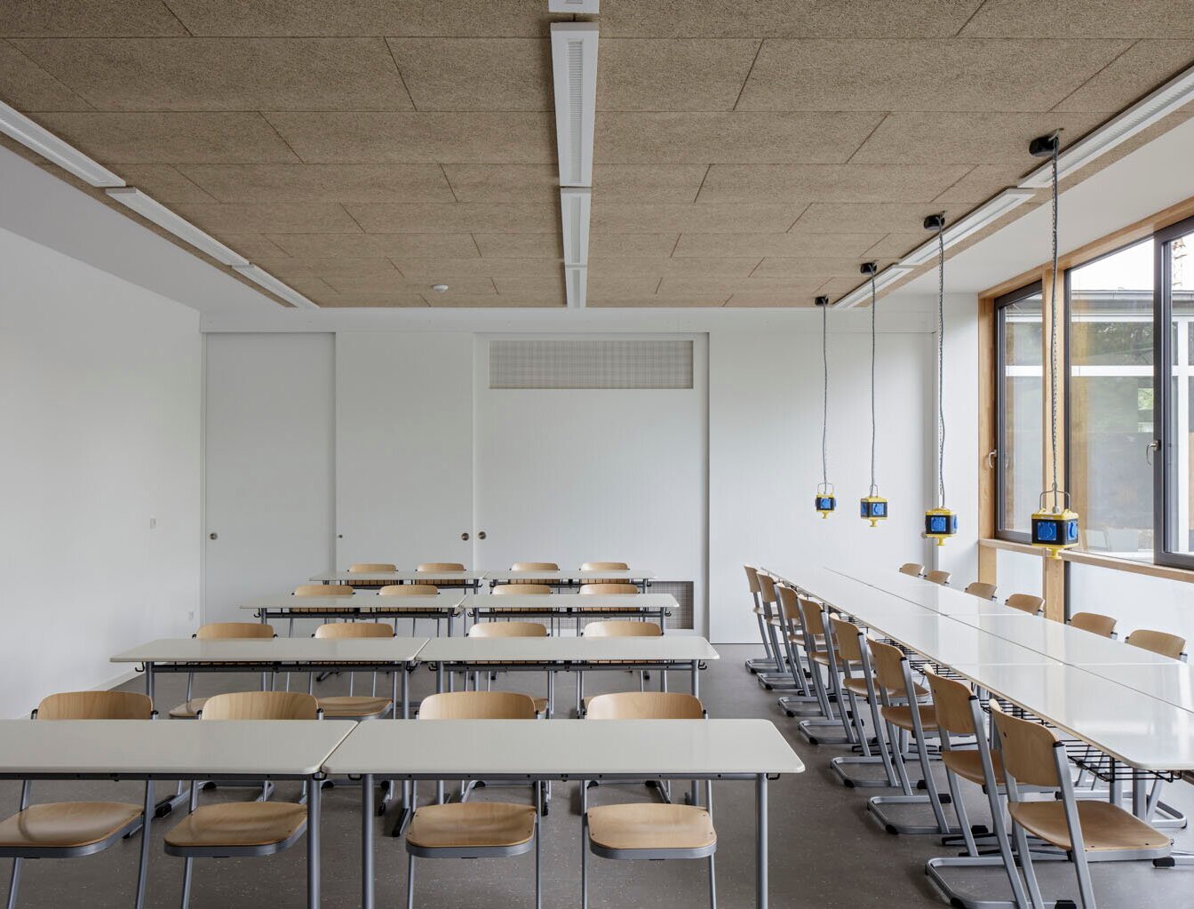Das Bild zeigt ein saniertes Klassenzimmer mit mehreren Tischreihen und -gruppen sowie Deckensteckdosen.