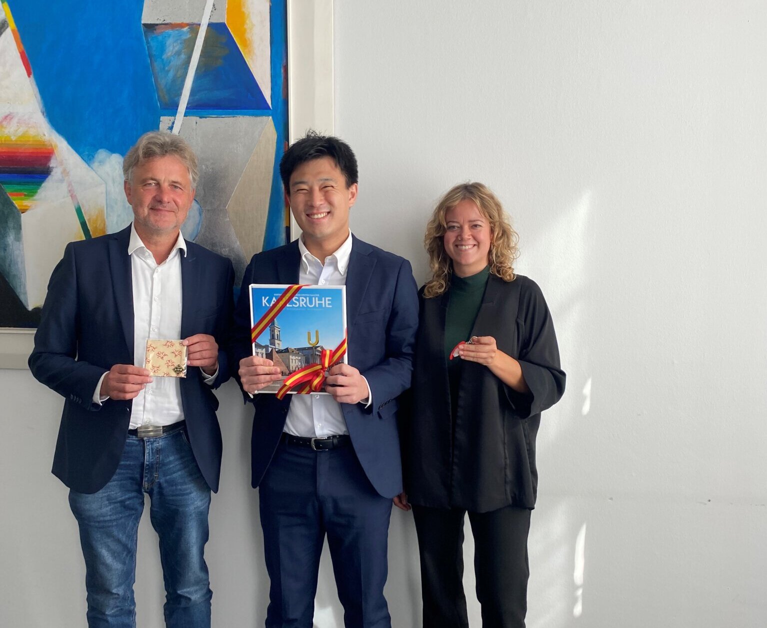 OB Frank Mentrup, So Takahashi und Daniela Burkhardt stehen vor einem Bild im Rathaus