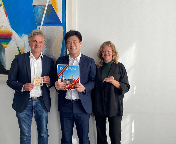 OB Frank Mentrup, So Takahashi und Daniela Burkhardt stehen vor einem Bild im Rathaus