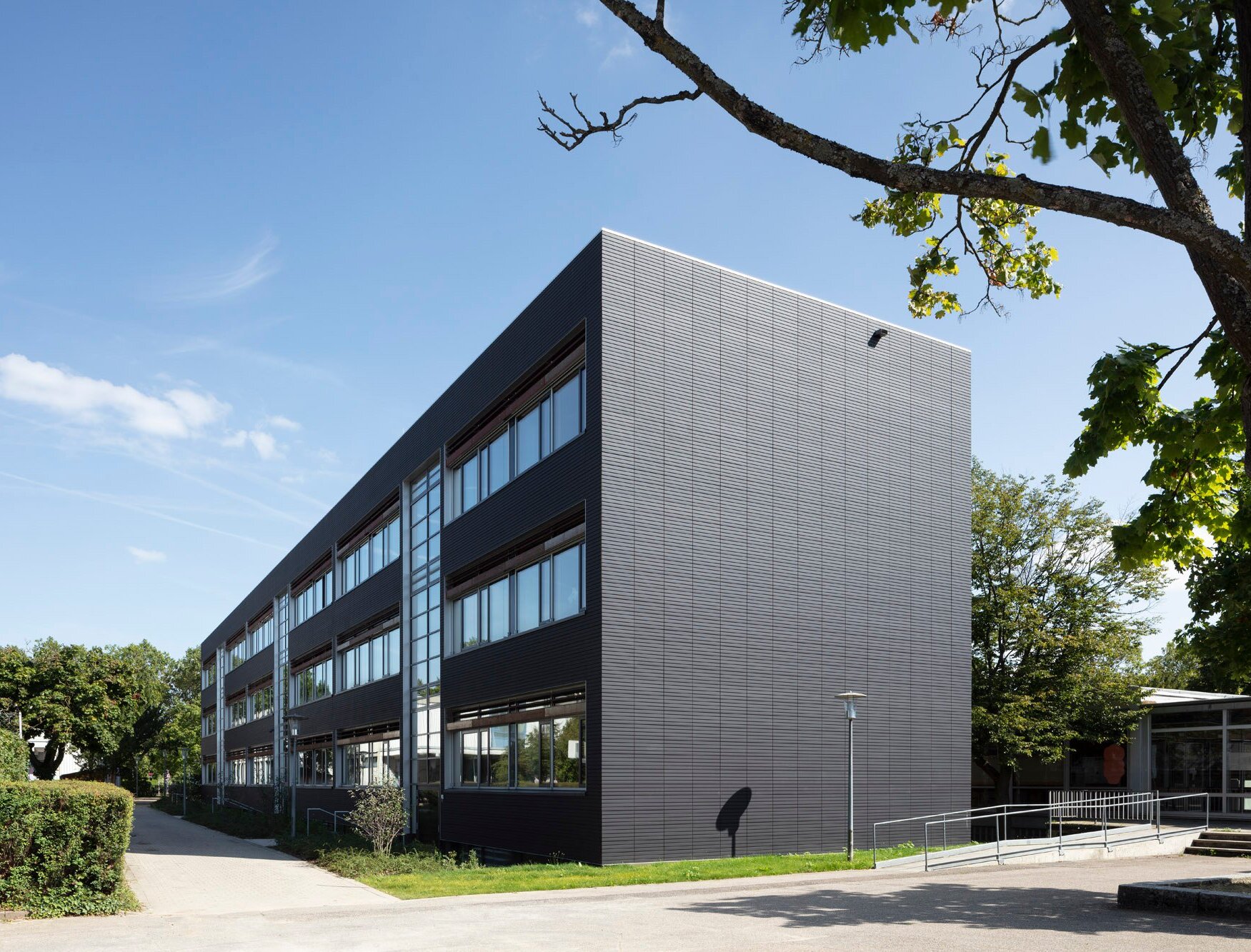 Das Bild zeigt die Nordostperspektive des Gebäudes mit einer anthrazitfarbenen Ziegelfassade und einem kleinen Verbindungsgang.